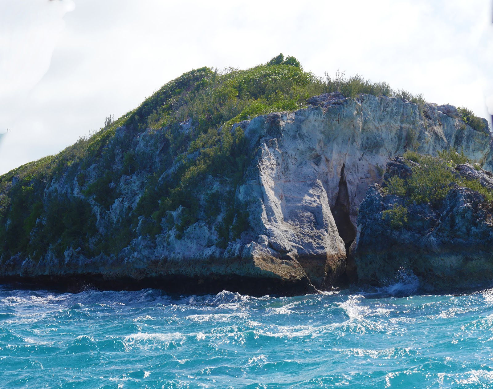 Exclusive Yachts - Close up of a rocky island with small waves crashing against the edge at Thunderball Grotto, Exuma Cays, Bahamas. The site is popular for tourists and has been a location for several movies.