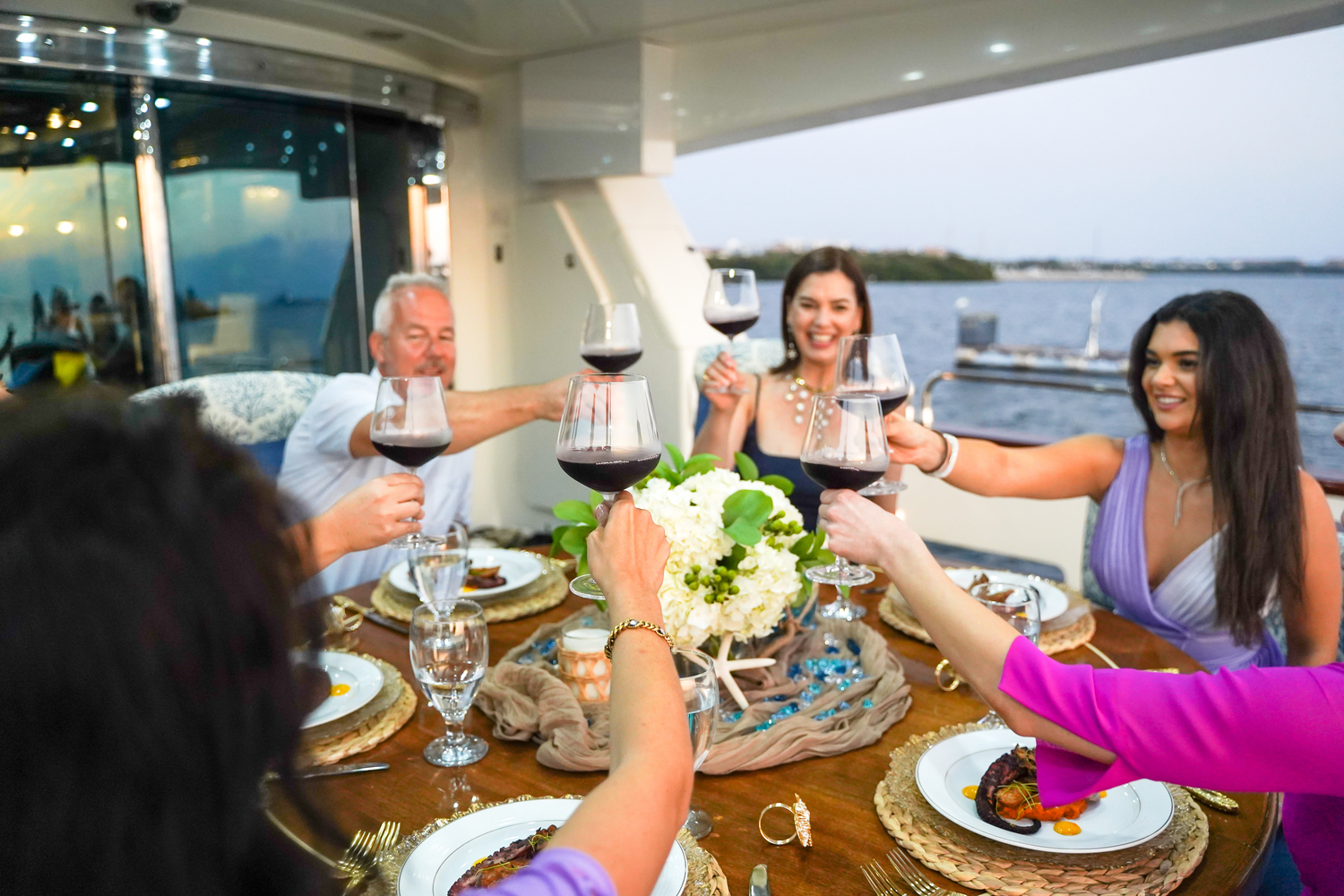 Star Sapphire Dining Aboard - Exclusive Yachts Exclusive Yachts - Guests aboard the MY Star Sapphire cheer with wine glasses, celebrating a memorable dining experience with an ocean backdrop.